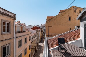 A narrow street with buildings on either side, featuring balconies and a wooden deck with a chair.