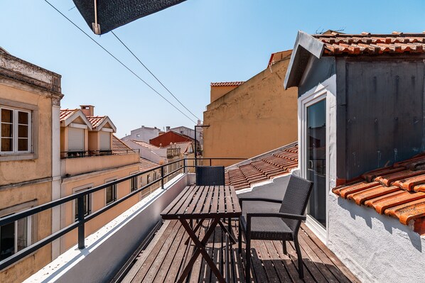 A balcony with a wooden table and chairs, a railing, and a view of neighboring buildings.