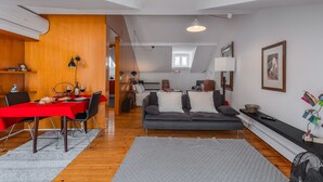 A modern living room with a dining area, a sofa, and a staircase leading to an upper level.