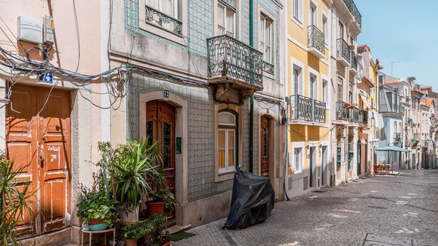 A quiet street with buildings, potted plants, and a covered table.