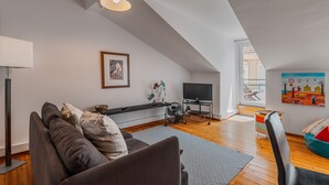 A modern loft apartment with a high ceiling, a sofa, a TV, and artwork on the walls.