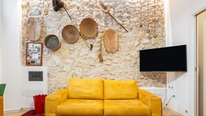 A yellow sofa in a room with a stone wall, a flat-screen TV, and various items hanging on the wall.