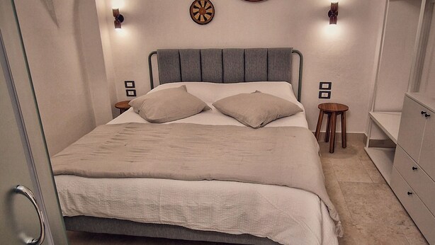 A bedroom with a bed, a small table, a chair, a wardrobe, and wall-mounted lights. - B&B La Casa Di Bianca (Manfredonia)