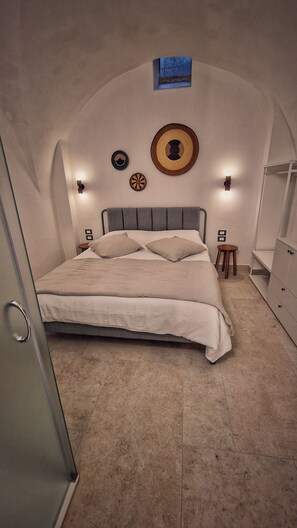 Un dormitorio con cama, una mesita, una silla, un armario y luces en la pared.
