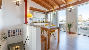 Une cuisine moderne avec des poutres en bois, un coin repas avec des chaises jaunes et une vue dégagée grâce à de grandes portes vitrées.