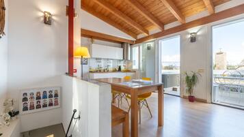 Une cuisine moderne avec des poutres en bois, un coin repas avec des chaises jaunes et une vue dégagée grâce à de grandes portes vitrées.