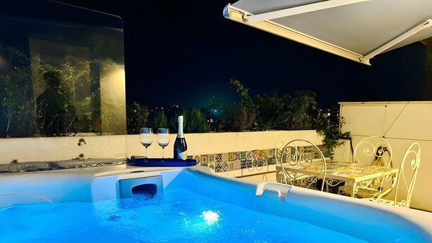 Un bain à remous avec une table et des chaises, une bouteille de champagne et un mur recouvert de carreaux.