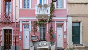 Un bâtiment rose avec un balcon, une porte verte et un banc à l’extérieur.