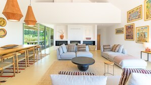 A modern living room with a dining area, sofas, a coffee table, pendant lights, and artwork on the walls.