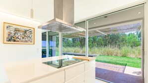 A modern kitchen with a glass cooktop, a stainless steel range hood, and a sliding glass door leading to an outdoor area.