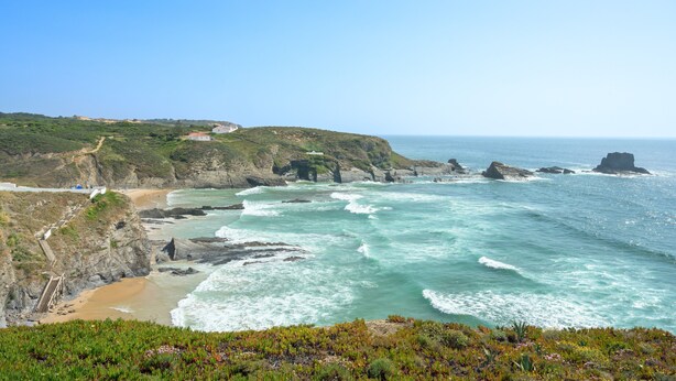 A coastal landscape with rocky cliffs, a beach, and a clear sky.
