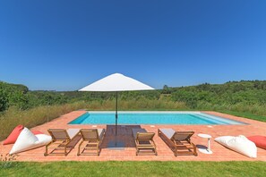 A swimming pool with lounge chairs and an umbrella, surrounded by greenery.
