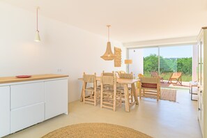 Une cuisine moderne avec des meubles blancs, une table à manger en bois, des chaises en osier et une vue sur l’extérieur.