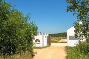 Un chemin de terre mène à un bâtiment blanc orné d’un logo et d’une enseigne indiquant un espace de camping.