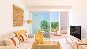 En moderne stue med sofa, en poselejr, fjernsyn og en skydedør, der fører ud til en udendørs terrasse.