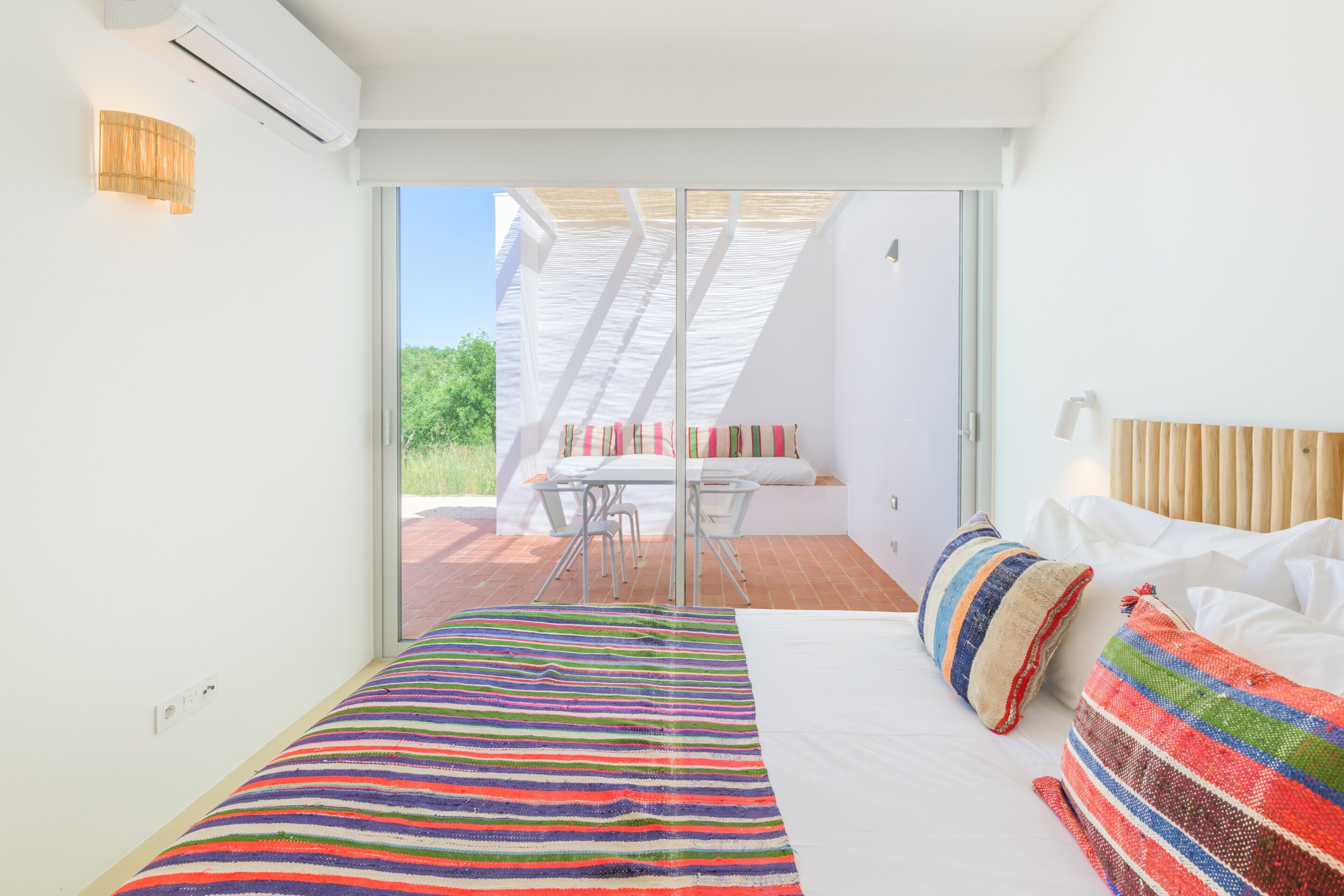 A bedroom with a bed, pillows, a window, and a view of an outdoor patio.