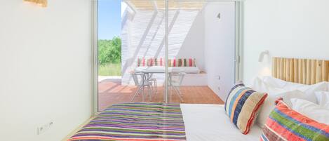 A bedroom with a bed, pillows, a window, and a view of an outdoor patio.