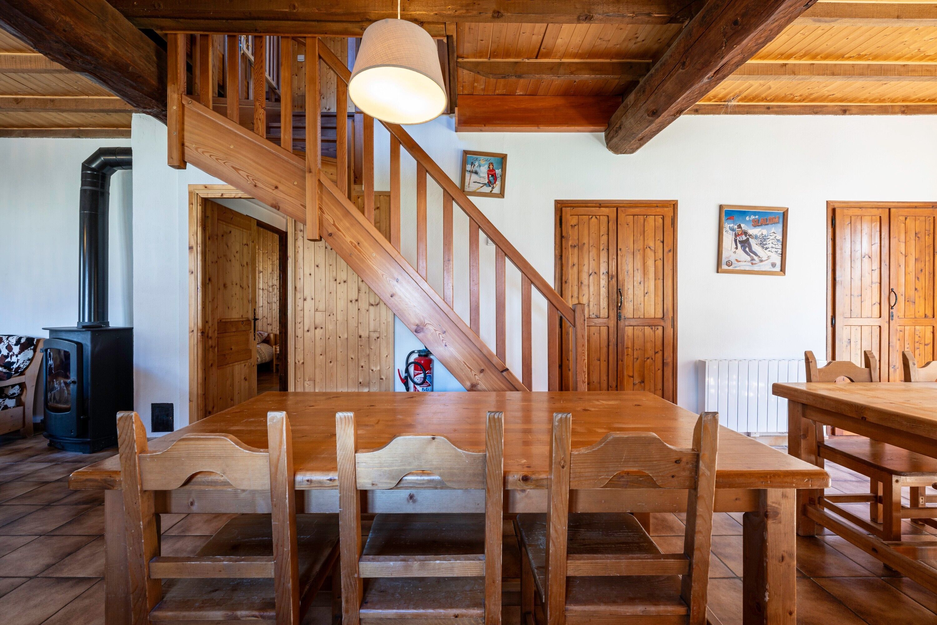 A wooden staircase leading to a second floor, a dining table with chairs, and a wooden ceiling.