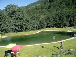 Un lac entouré d’une végétation luxuriante, un espace pique-nique avec une table et des chaises, et un sentier pédestre.