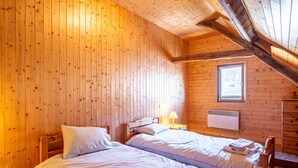 A wooden cabin bedroom with two beds, a window, and a wall-mounted heater. - Chalet 'Savoiage' with Mountain View, Private Terrace and Wi-Fi (Saint-Colomban-des-Villards)