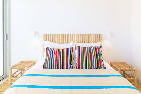 A bed with striped pillows, a wooden headboard, and two bedside tables with woven stools.