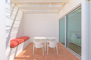 A small patio with a white table and chairs, a red bench, and a glass door leading to a bedroom. - Holiday Home 'Casa Do Regadio - Casa 3' with Private Pool, Wi-Fi and Air Conditioning (Zambujeira do Mar)