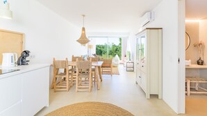 Een moderne keuken met witte kasten, een eethoek met houten stoelen, een hanglamp en een uitzicht door grote ramen.