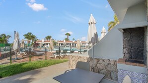 A patio area with a table and chairs, a stone fireplace, and a pool with lounge chairs and umbrellas. - 'Vista' with Shared Pool, Wi-Fi and Air Conditioning (Maspalomas)