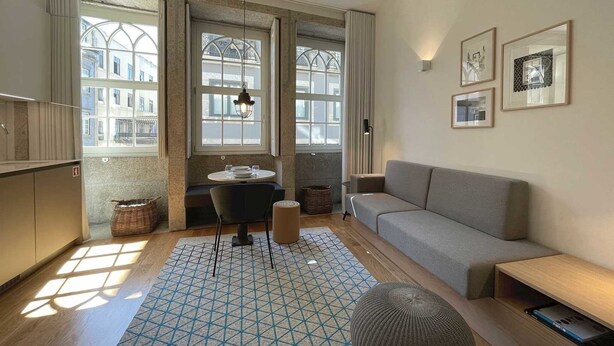 Un salon moderne avec un canapé gris, une table à manger avec des chaises et un tapis à motifs.