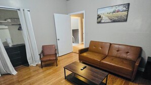 Una sala de estar con un sofá de cuero marrón, una mesa de centro de madera, un sillón marrón y un cuadro en la pared.
