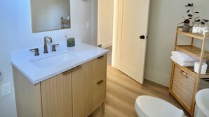 A modern bathroom with a white sink, mirror, and toilet. There is a wooden vanity and a shelf with towels. - Next Level Convenience in Grand Rapids premier neighborhood (Grand Rapids)
