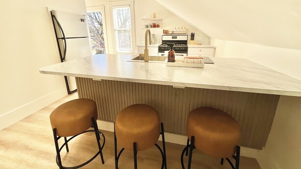 A kitchen with a large island, a refrigerator, a stove, and three bar stools. - Next Level Convenience in Grand Rapids premier neighborhood (Grand Rapids)