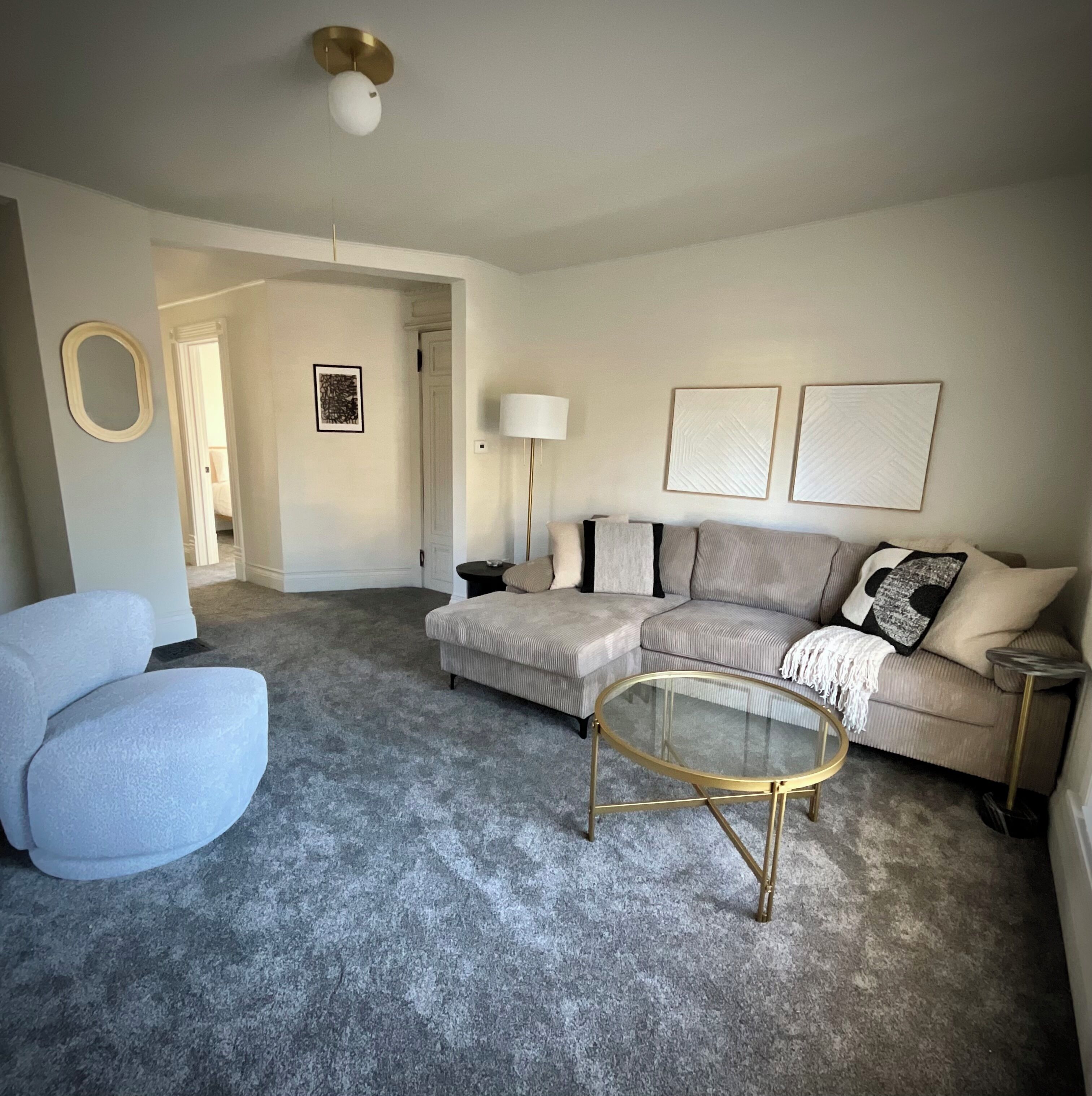 A living room with a grey carpet, a round glass coffee table, a sofa, and a side table.