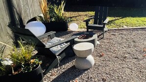 A patio area with outdoor seating, including a wooden chair and a lounge chair, surrounded by potted plants and a fire pit. - Next Level Convenience in Grand Rapids premier neighborhood (Grand Rapids)