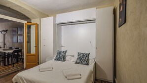 Et hotelværelse med en seng, to puder, et natbord, et skab og et lille spiseområde med stole og et bord.
