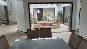 A modern dining area with a glass table and cushioned chairs, a spiral staircase, and a view of an outdoor garden with plants and a seating area. - House in Gated Community in Peruíbe-SP (Boungaiville Peruíbe)