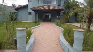 A pathway leading to a building with a tiled roof and a covered entrance. - House in Gated Community in Peruíbe-SP (Boungaiville Peruíbe)