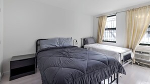 Un dormitorio con dos camas, una mesita de noche, una lámpara y un ventanal con cortinas.