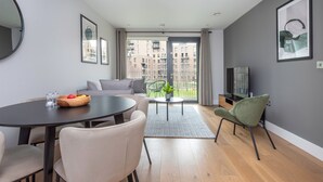 Uma sala de estar moderna com uma mesa de jantar, cadeiras, um sofá, uma TV e uma varanda com vista para edifícios.