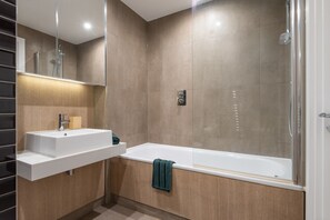 Un baño moderno con lavamanos, espejo y bañera.