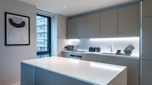 Cozinha moderna com ilha central, eletrodomésticos embutidos e vista para a cidade através de uma janela.