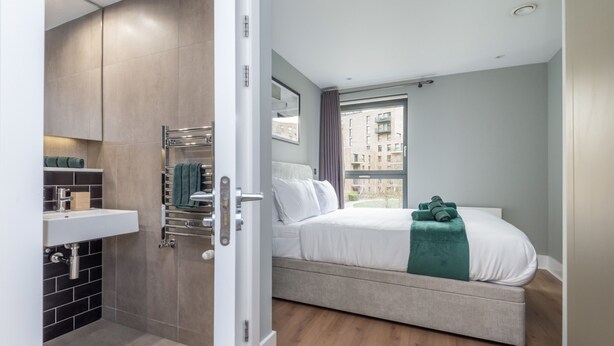 Quarto com cama, banheiro com pia e vista para edifícios.