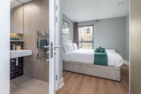 Un dormitorio con cama, un baño con lavabo y vista a edificios.
