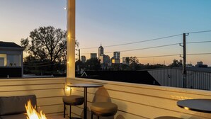 A rooftop patio with a fire feature, seating, and a city skyline view.
