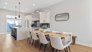 A modern kitchen with white cabinets, a central island with bar stools, and a dining area with a wooden table and white chairs.