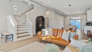 A modern living room with a staircase, leather sofa, and a dining area.