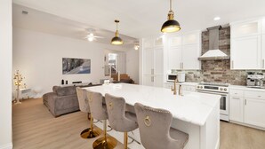 A modern kitchen with white cabinets, a large island with bar stools, and a stone backsplash.