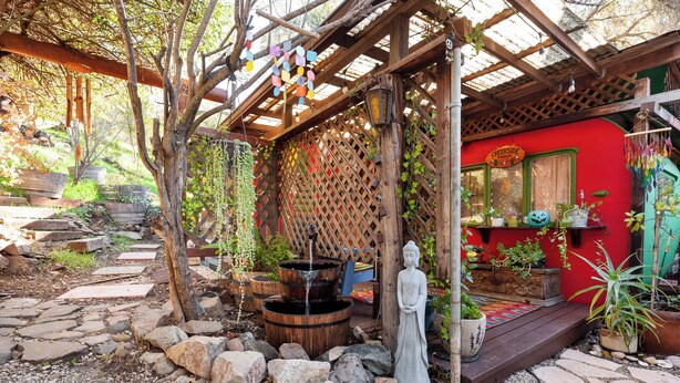 A garden with a wooden pergola, a stone pathway, a water feature, and a statue.