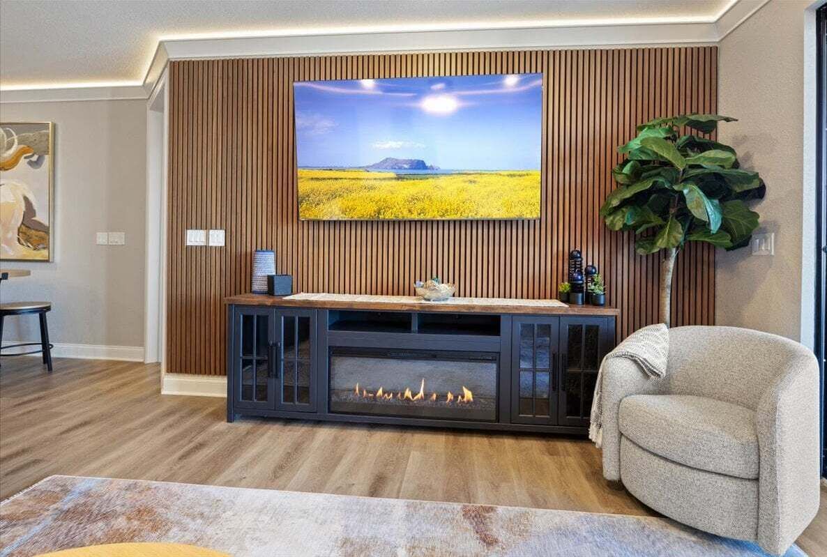 Ein Wohnzimmer mit Flachbildfernseher an einer Holzwand, einem Kamin darunter und einer großen Pflanze zur Rechten.