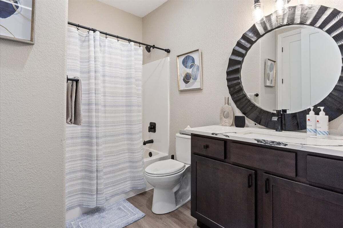 A bathroom with a shower curtain, toilet, sink with a mirror, and a towel rack.